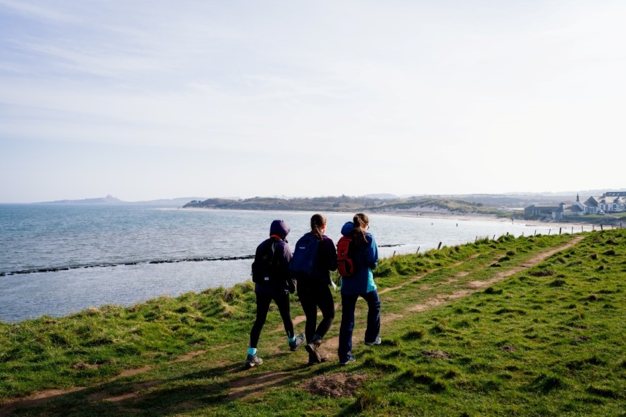 three girls walk along Northumberland Coast Path overlooking the sea